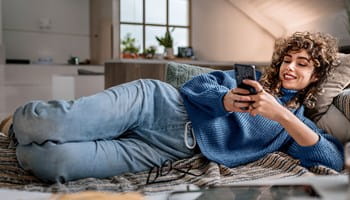 Femme dans sa maison qui souscrit l'assurance habitation en ligne sur son téléphone.