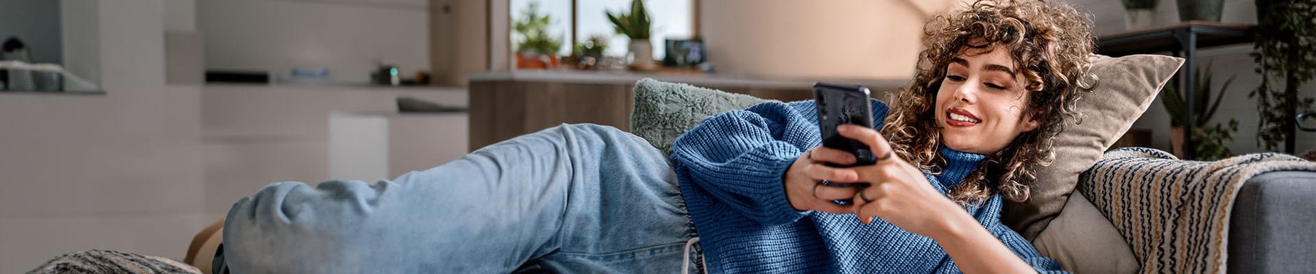 Femme dans sa maison qui souscrit l'assurance habitation en ligne sur son téléphone.