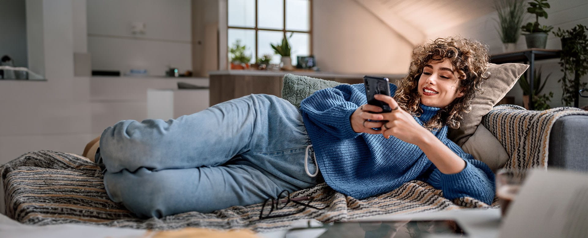 Femme dans sa maison qui souscrit l'assurance habitation en ligne sur son téléphone.