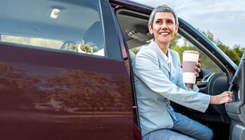 Femme appuyée contre sa voiture, sereine, rassurée par son assurance Auto.