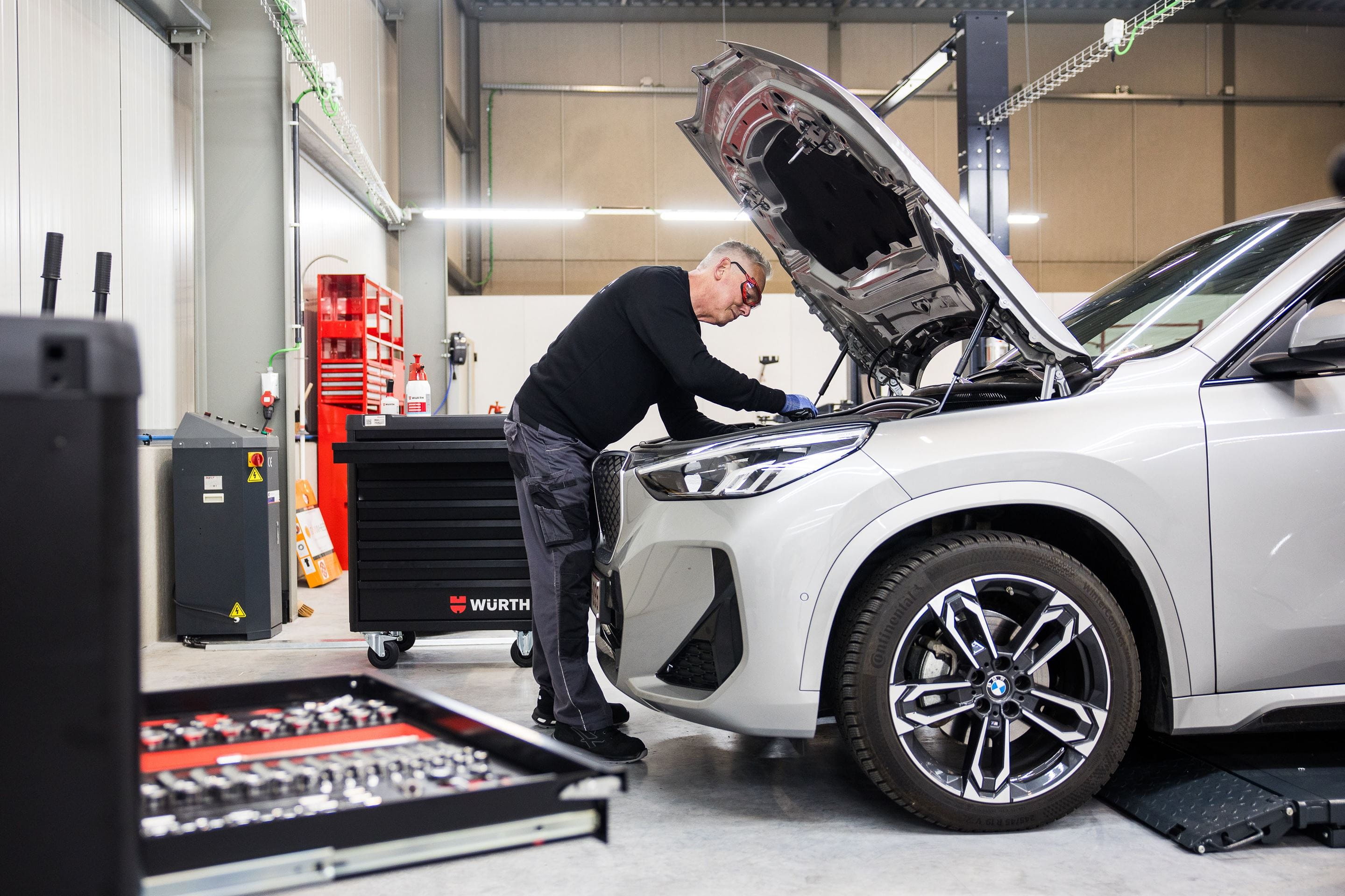 Technicien en train d’inspecter et réparer un moteur sous le capot d’une voiture dans un atelier AXA Fast Car Repair