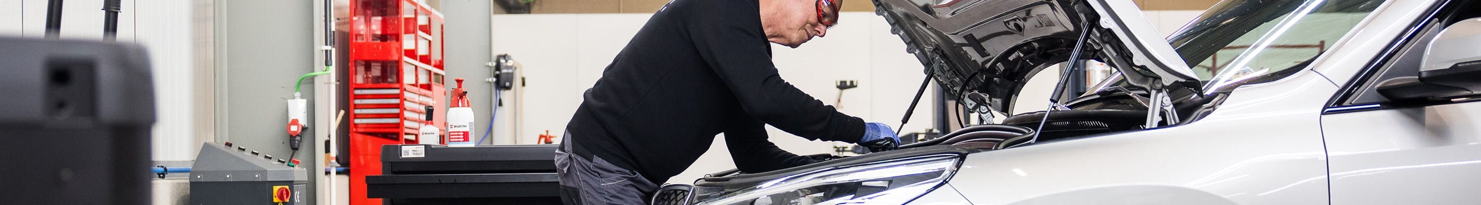 Technicus die een automotor onder de motorkap controleert en herstelt in een AXA Fast Car Repair-werkplaats
