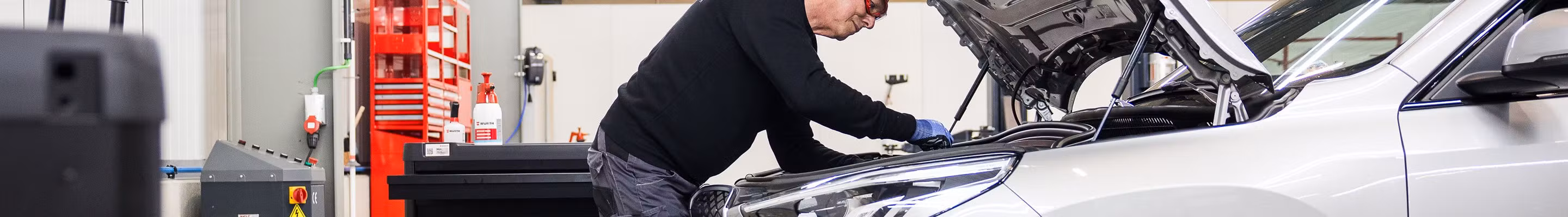 Technicien en train d’inspecter et réparer un moteur sous le capot d’une voiture dans un atelier AXA Fast Car Repair