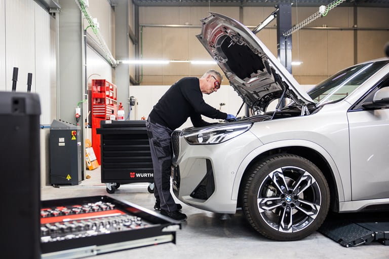 Technicien en train d’inspecter et réparer un moteur sous le capot d’une voiture dans un atelier AXA Fast Car Repair