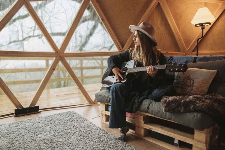 Une femme à jouer de la guitare séance sur un canapé dans un maison alternative (tiny house)
