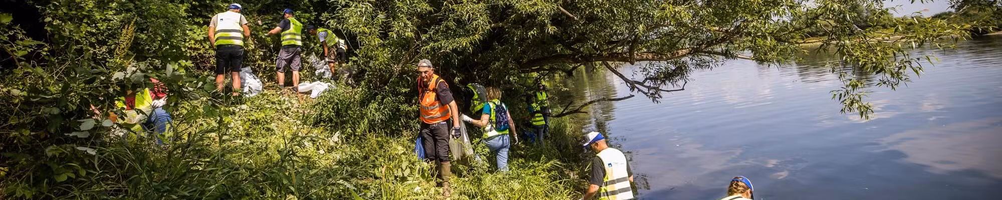 Volontaires équipés nettoyant les berges d’une rivière après une inondation, retirant des déchets dans l’eau et sur les rives en équipe.